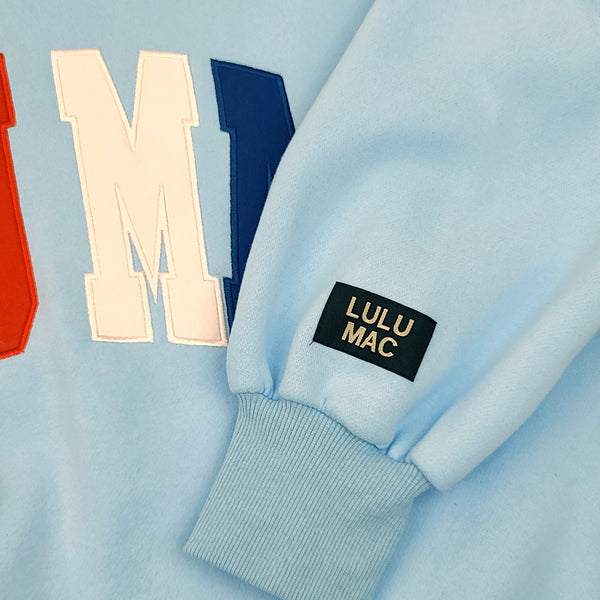 Light blue sweater with 'LULU MAC' label on a light blue background