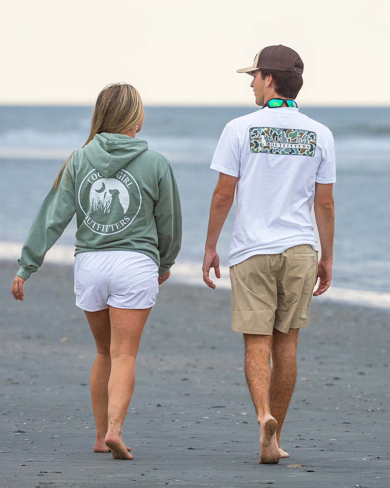 Two people walking on the beach wearing Local Boy and Local Girl clothing.