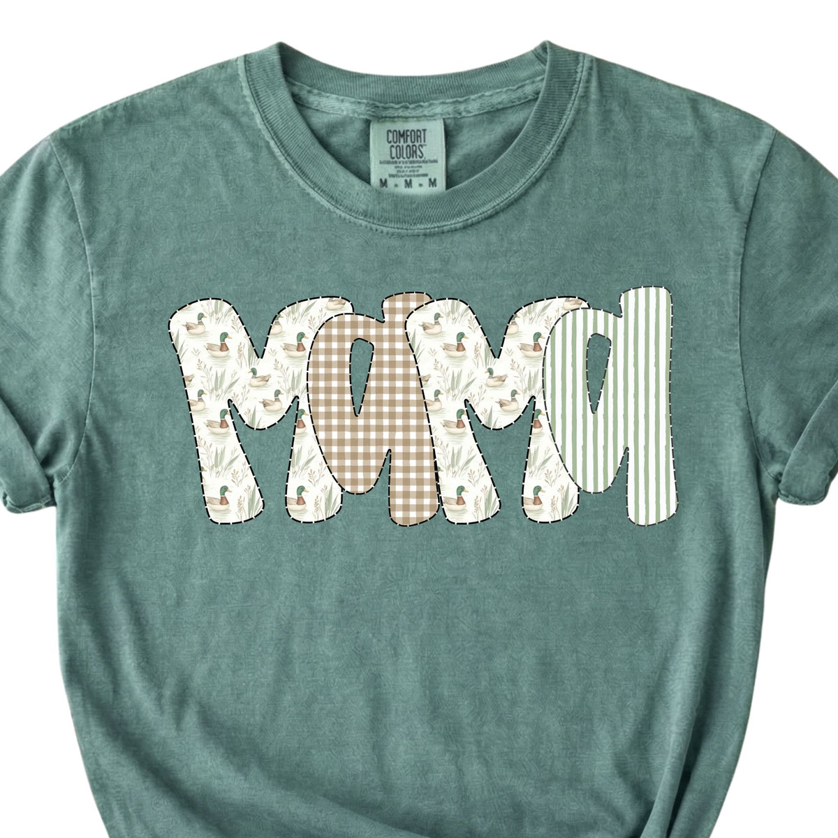 Light green t-shirt with “Mama” patchwork graphic on front, styled with rolled sleeves and knotted hem.