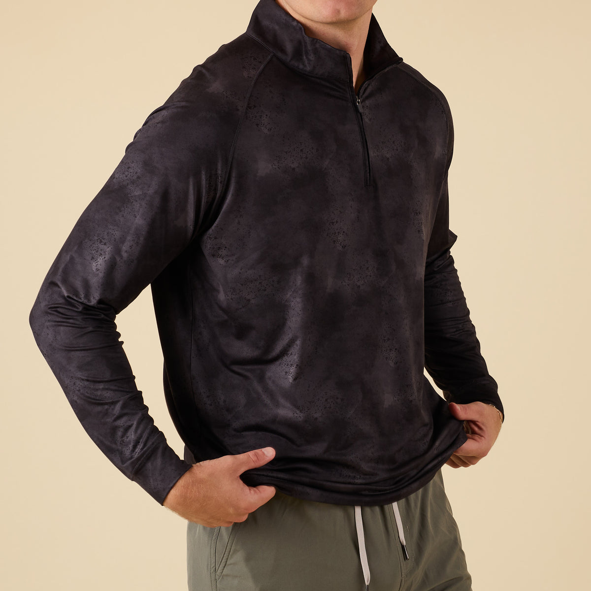 Side angle view of men’s black camo performance quarter-zip with model holding hem.