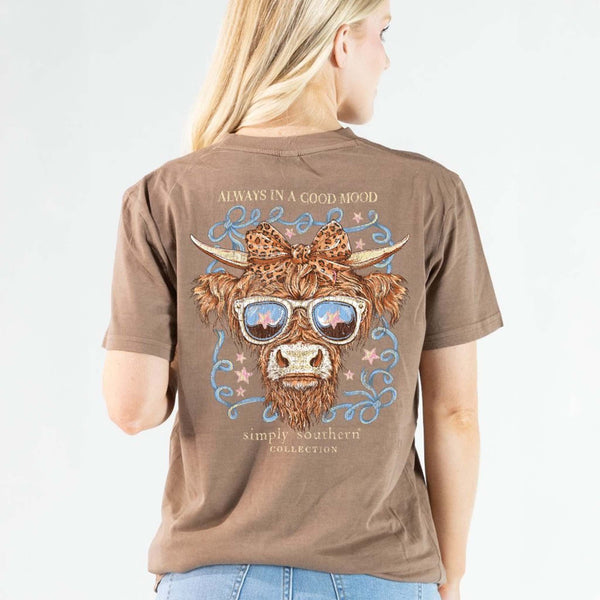 Brown t-shirt with a cow graphic and text worn by a person on a light gray background