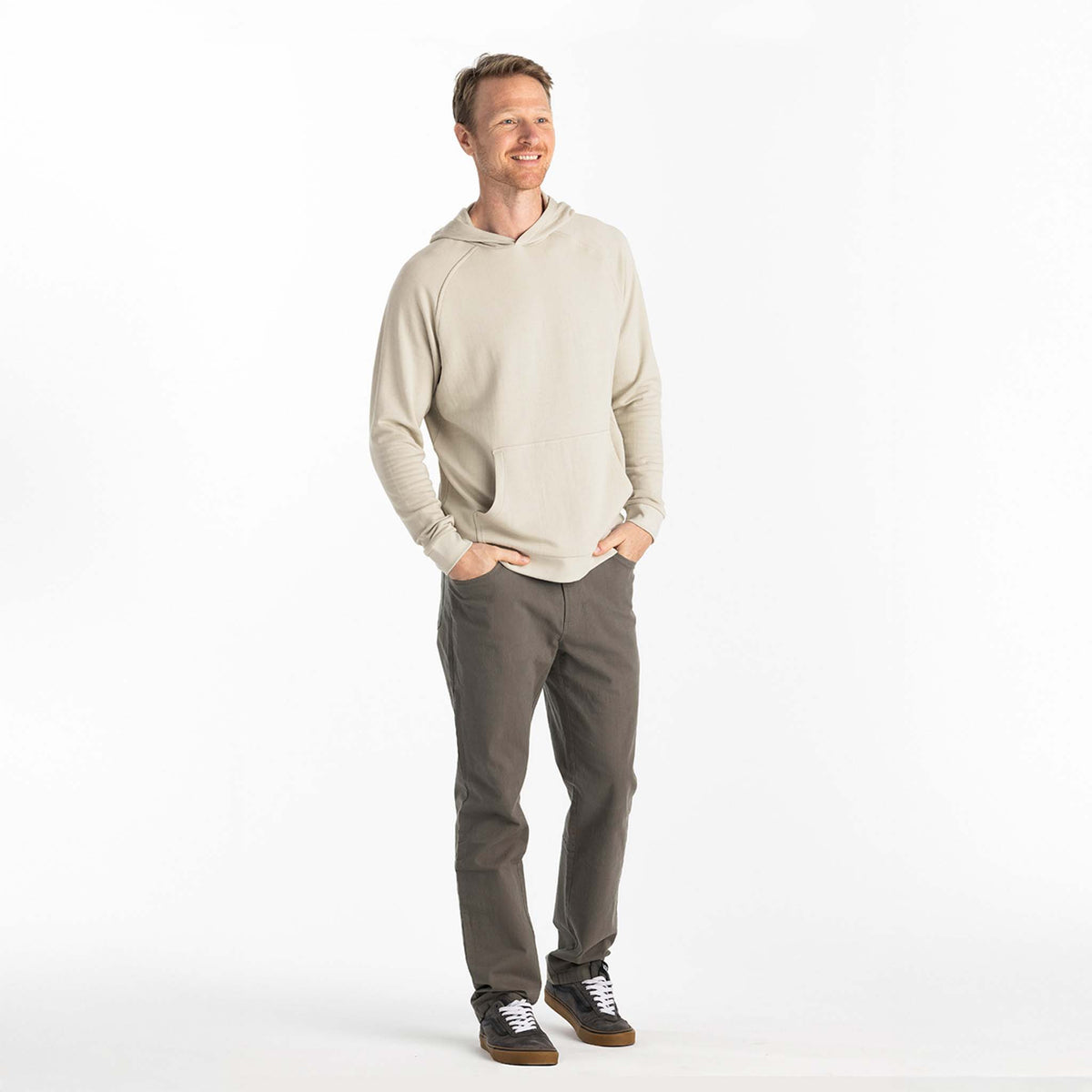 Man wearing a beige hoodie and gray pants on a white background