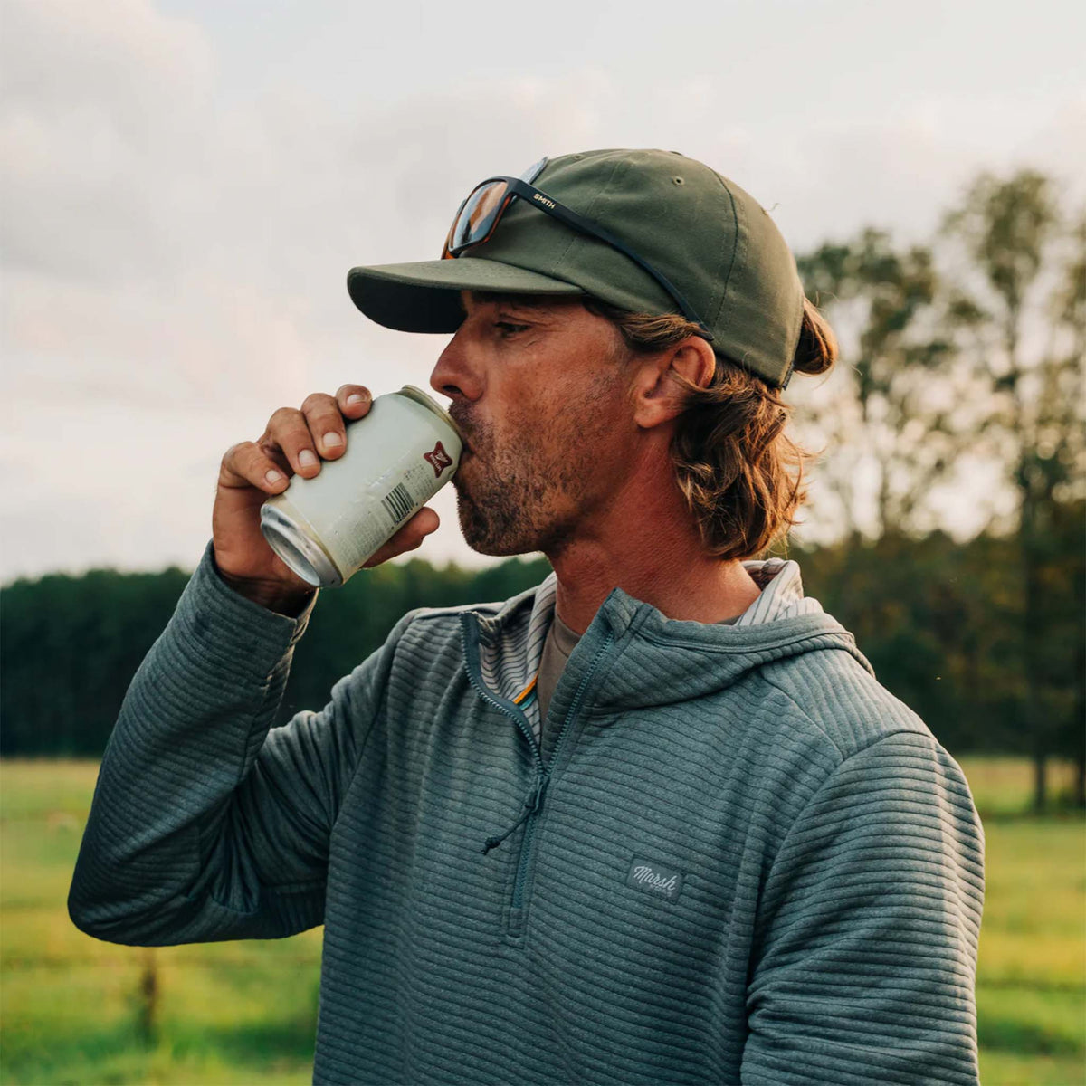 Man drinking from a can in a field with trees in the background