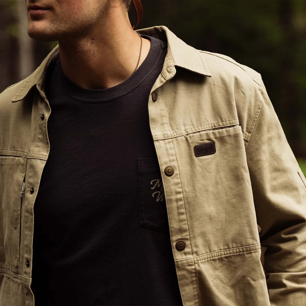 Man wearing a slate green jacket over a black shirt with a blurred background