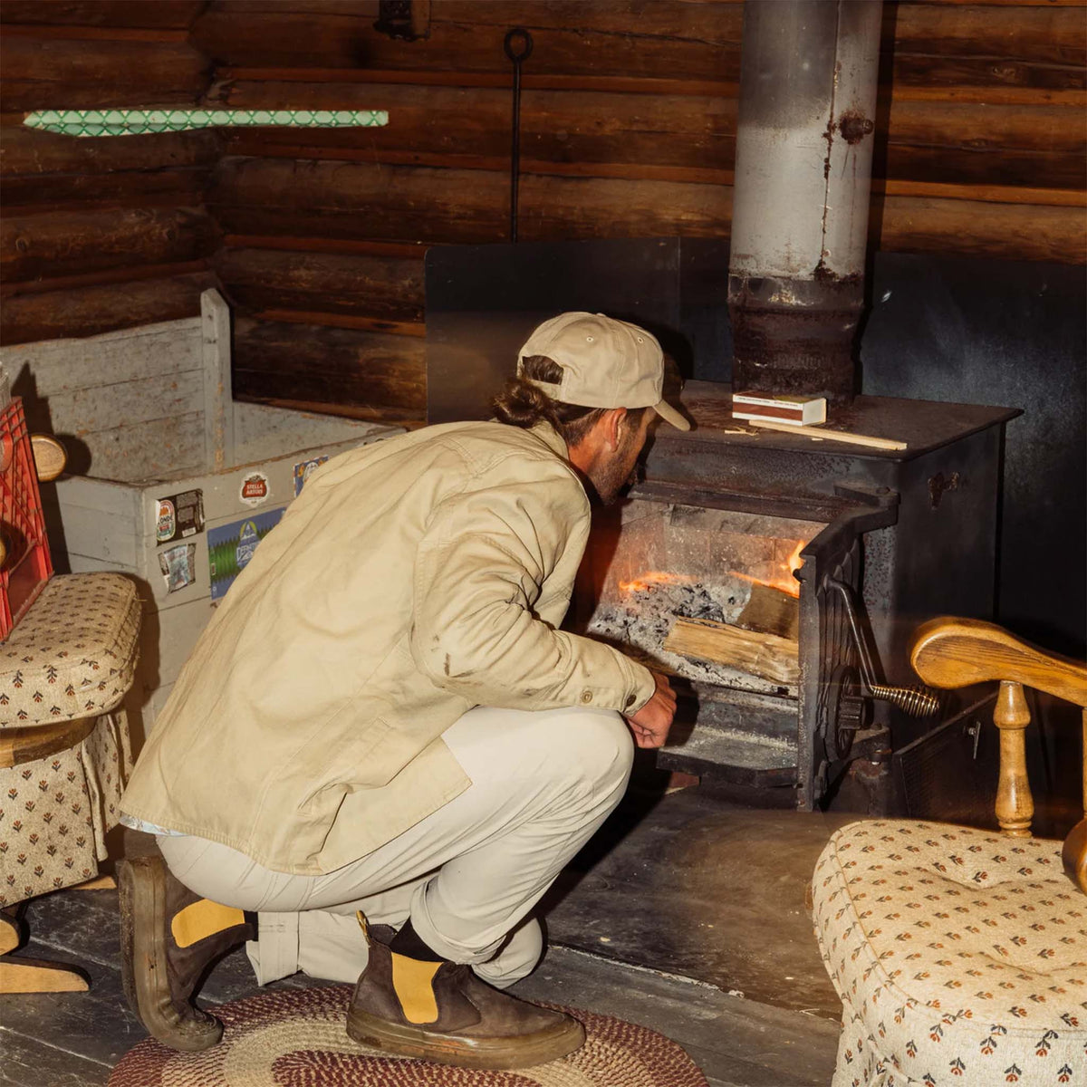 Man tending to a wood stove in a rustic cabin interior.