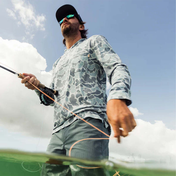 Marsh Wear Buxton Tech Hoodie in Camo, sizes S-XXL. Lifestyle shot of man fishing in silver mallard camo hoodie with rod extended over water.
