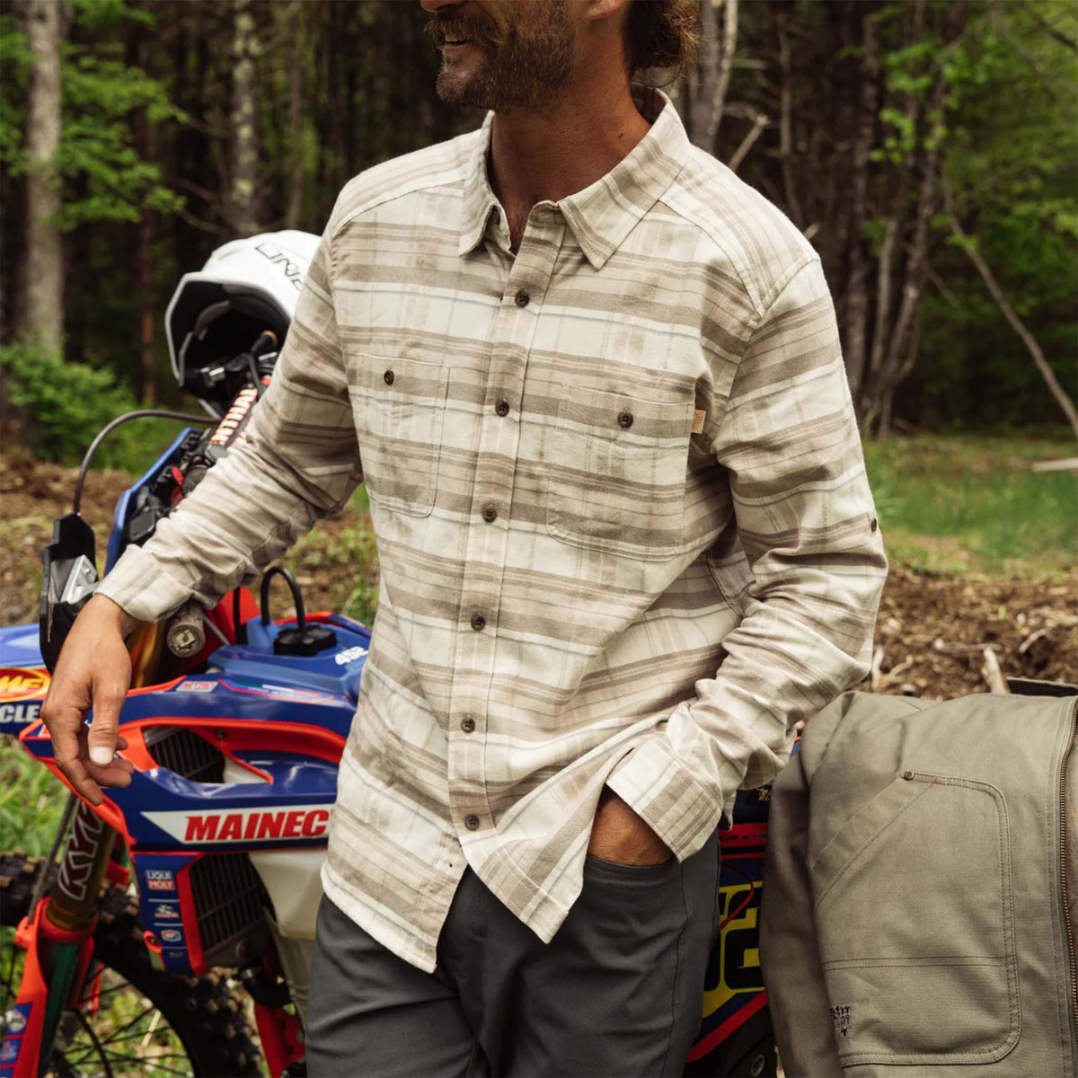 Man wearing a plaid shirt standing next to an ATV in a forest setting