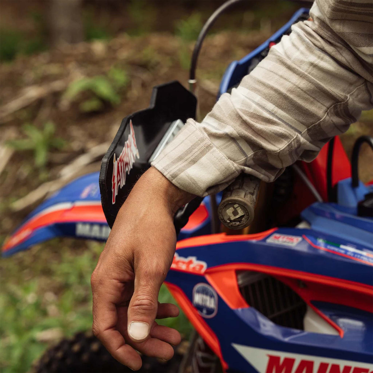 Close-up of a hand on a red and blue ATV with a blurred natural background