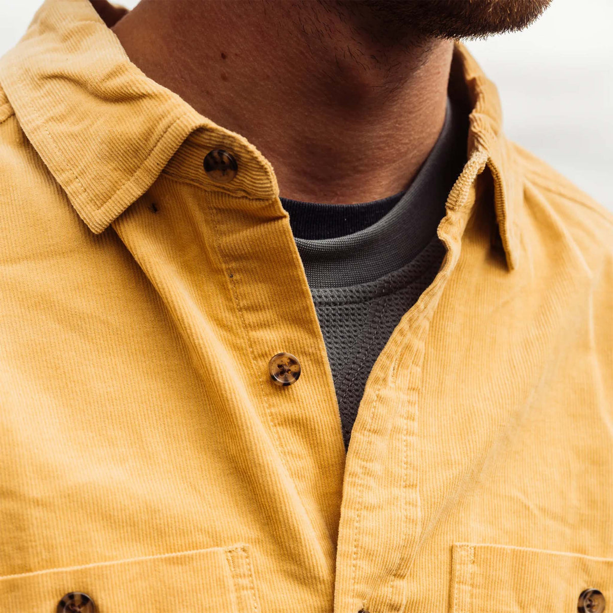 Close-up of a mustard yellow shirt with a person wearing it, focusing on the collar and buttons.