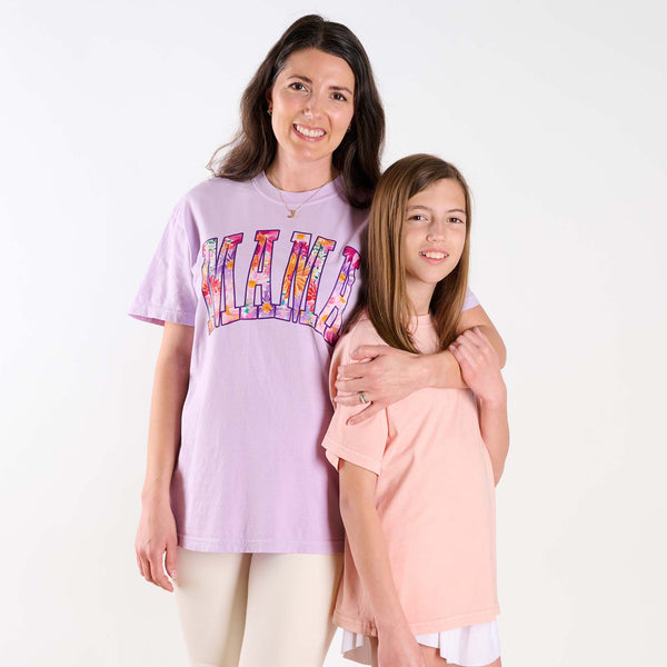 Woman and young girl standing together, woman wearing a light purple t-shirt with colorful text design.