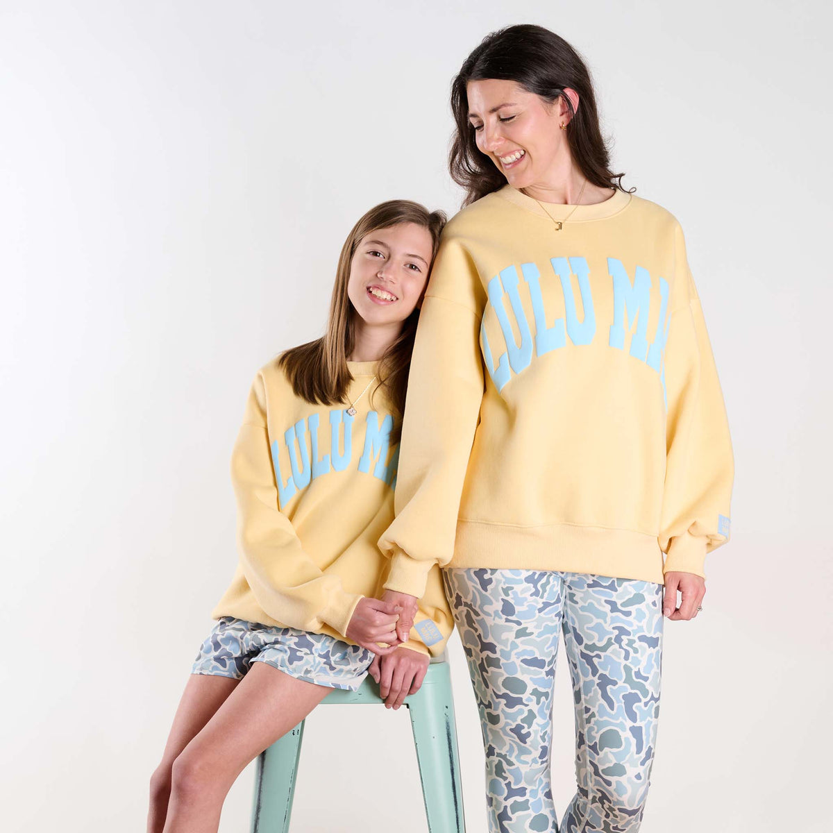 Two people wearing matching yellow sweatshirts with 'LULU MAC' text on a white background.