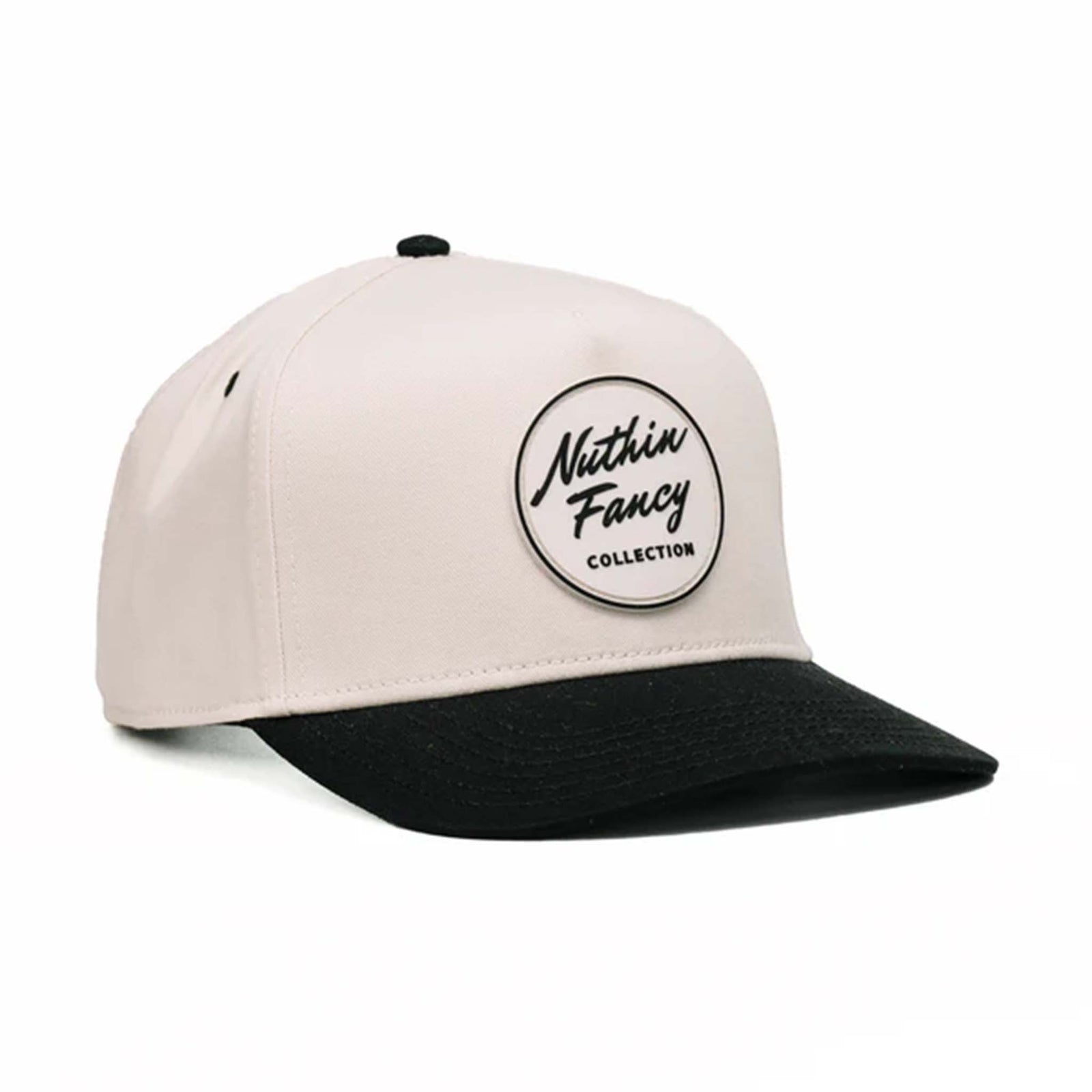 Two-toned 5-panel high crown trucker hat with an off-white front and black pre-curved bill. Features an off-white and black rubber 'Nuthin’ Fancy' patch on the front, black mesh back panels, and an adjustable plastic snapback closure. One size fits most.