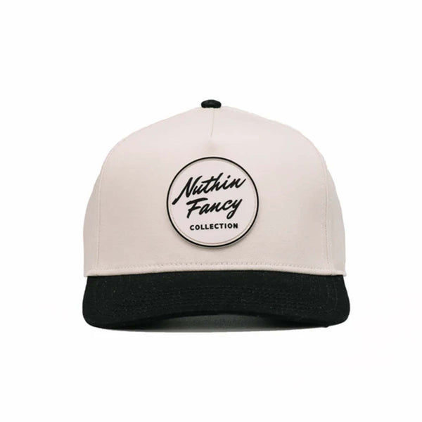 Two-toned 5-panel high crown trucker hat with an off-white front and black pre-curved bill. Features an off-white and black rubber 'Nuthin’ Fancy' patch on the front, black mesh back panels, and an adjustable plastic snapback closure. One size fits most.
