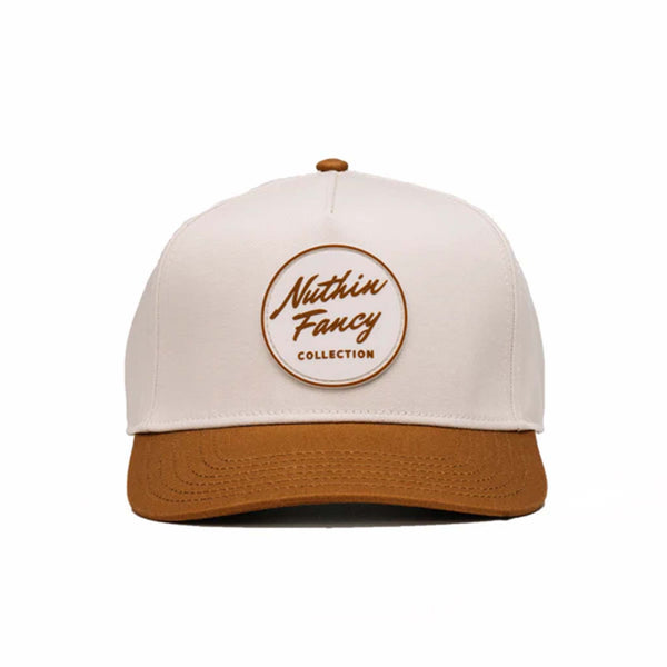 Two-toned 5-panel high crown trucker hat with an off-white front and rust-colored pre-curved bill. Features an off-white and rust rubber 'Nuthin’ Fancy' patch on the front, rust mesh back panels, and an adjustable plastic snapback closure. One size fits most.
