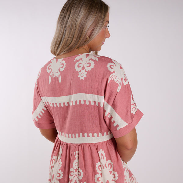  Woman wearing a pink dress with white patterns on a plain background