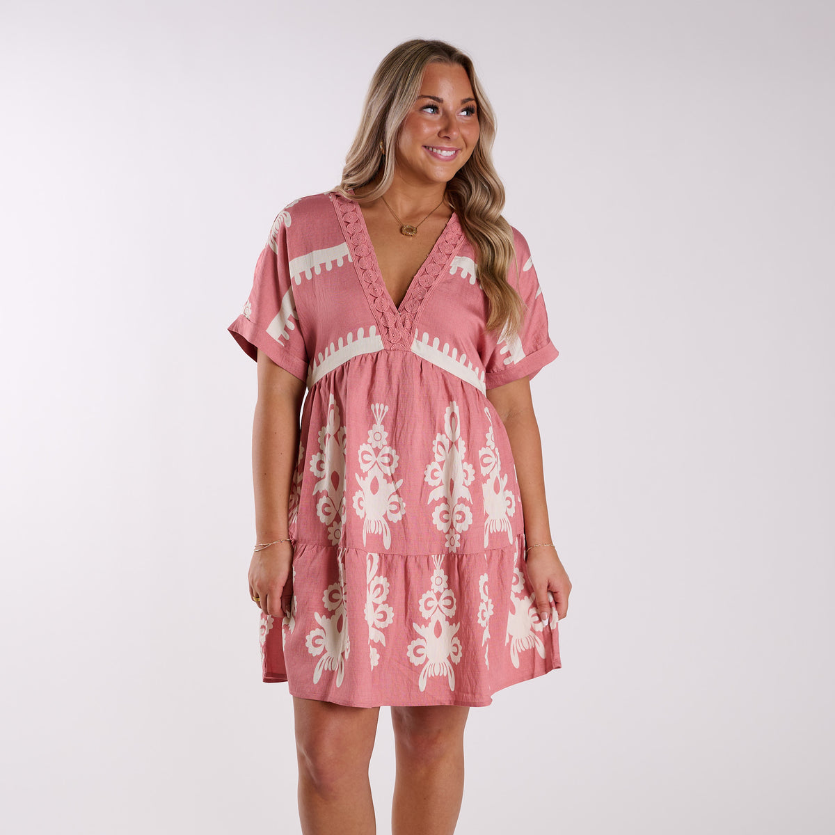 Blush | Woman wearing a pink dress with white patterns on a plain background