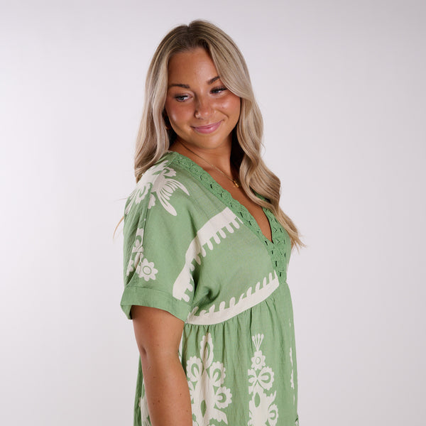  Woman wearing a green dress with white patterns on a plain background