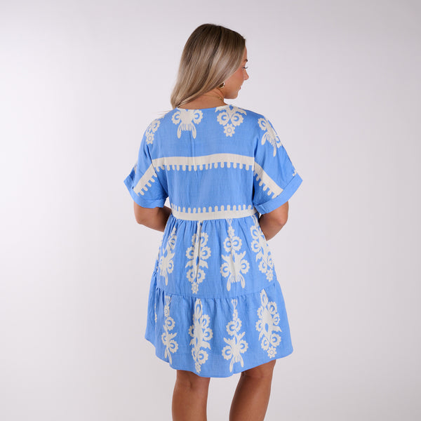  Woman wearing a blue dress with white embroidery on a plain background