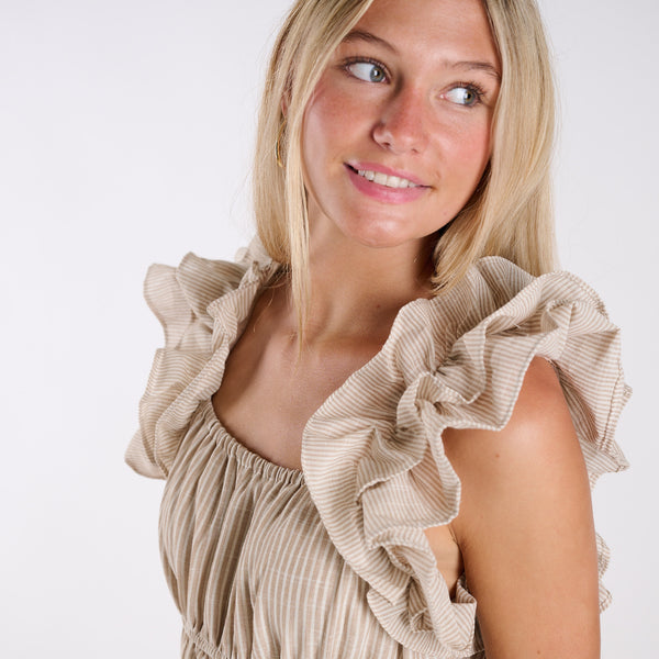  Woman wearing a beige dress with ruffled shoulders against a white background