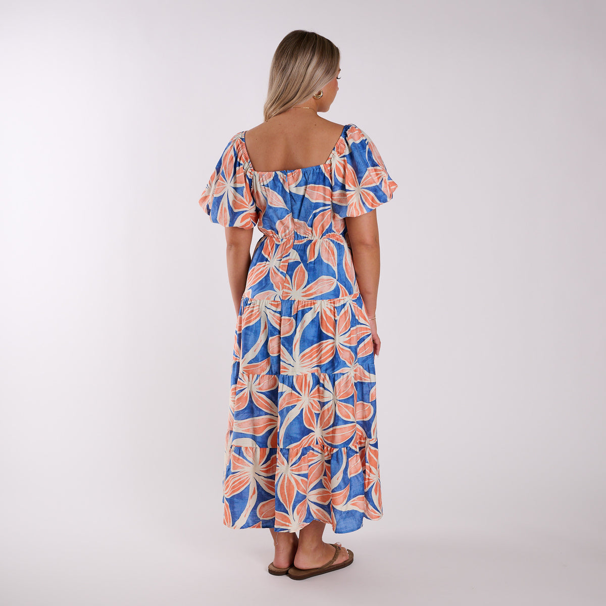 Back view of a Woman wearing a blue and orange floral dress on a white background