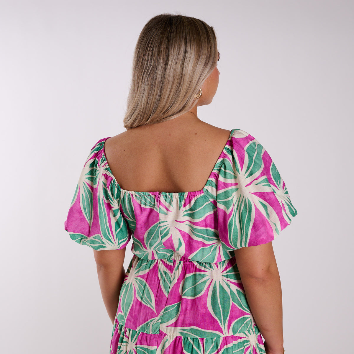 Woman wearing a pink and green floral dress against a white background