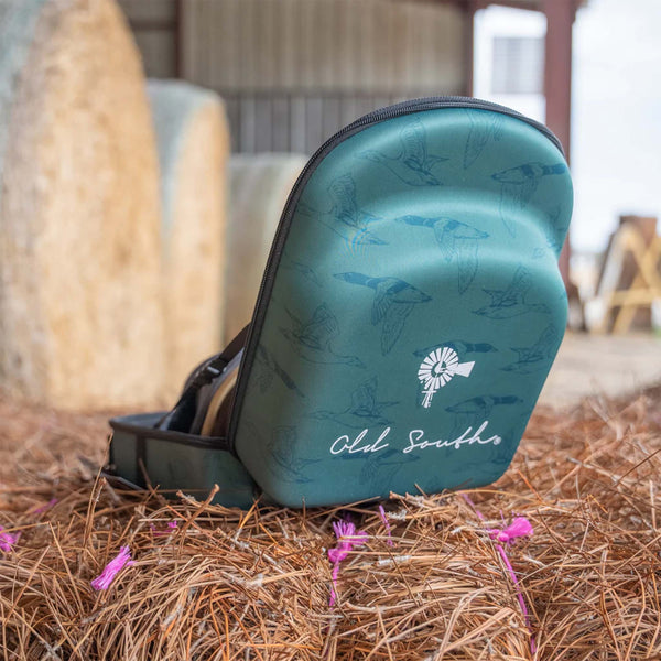 Old South 6 Hat Travel case is green duck pattern.
Angled side view of the open Old South Duck Pattern Hat Case resting on pine straw, showing the illustrated duck pattern, black zipper, and “Old South” branding in white cursive, with a barn setting in the background.