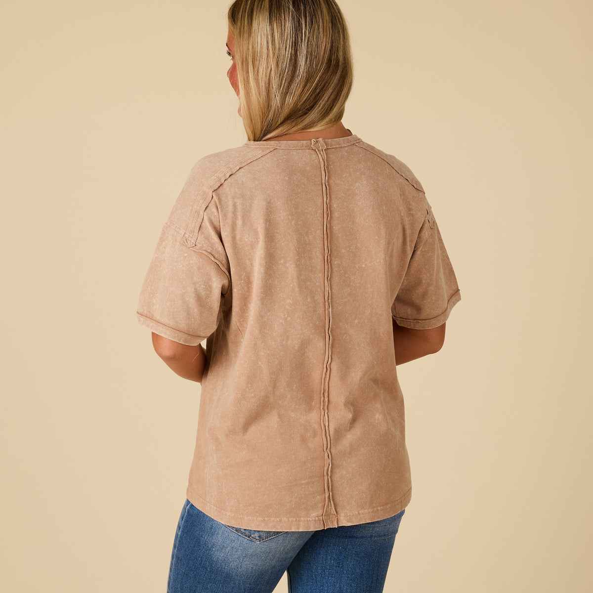 Person wearing a beige shirt and blue jeans on a beige background