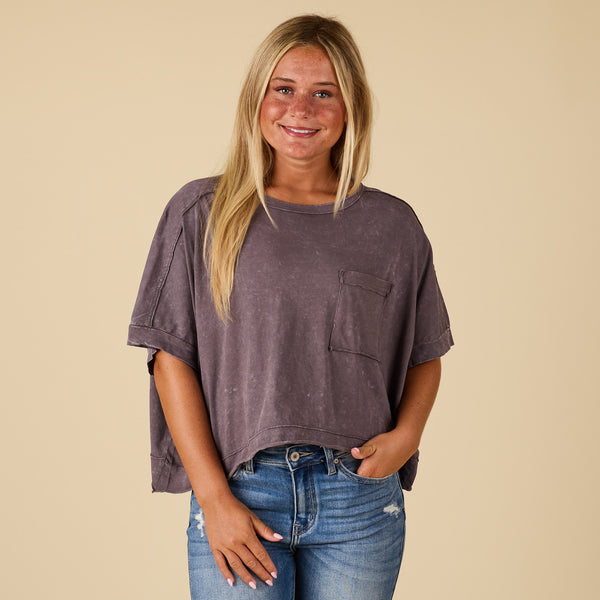  Woman wearing a charcoal grey t-shirt and blue jeans against a beige background