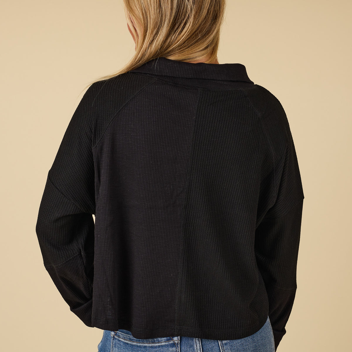 Person wearing a black ribbed sweater against a beige background