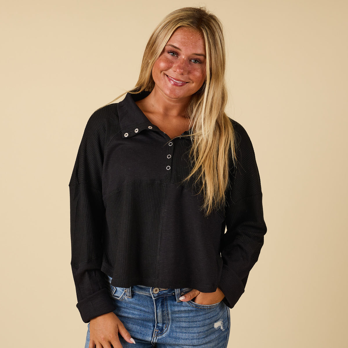 Woman wearing a black long-sleeve shirt with buttons and blue jeans on a beige background