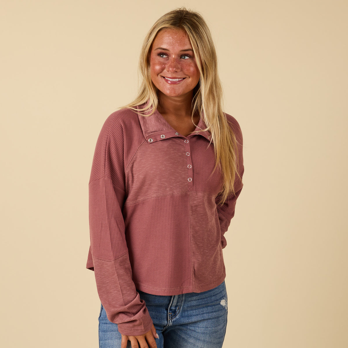Woman wearing a pink long-sleeve shirt and blue jeans against a beige background