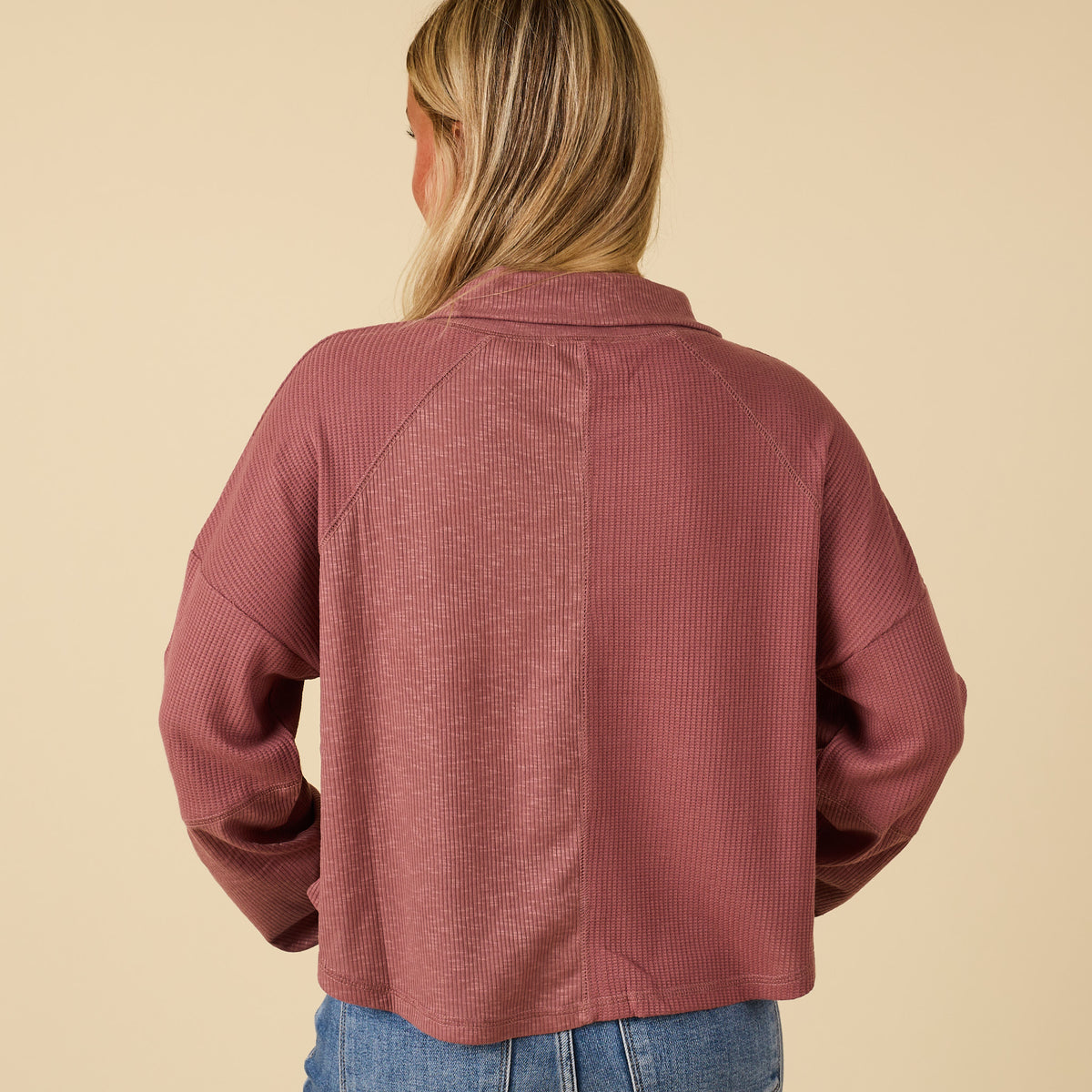 Person wearing a maroon textured jacket on a beige background