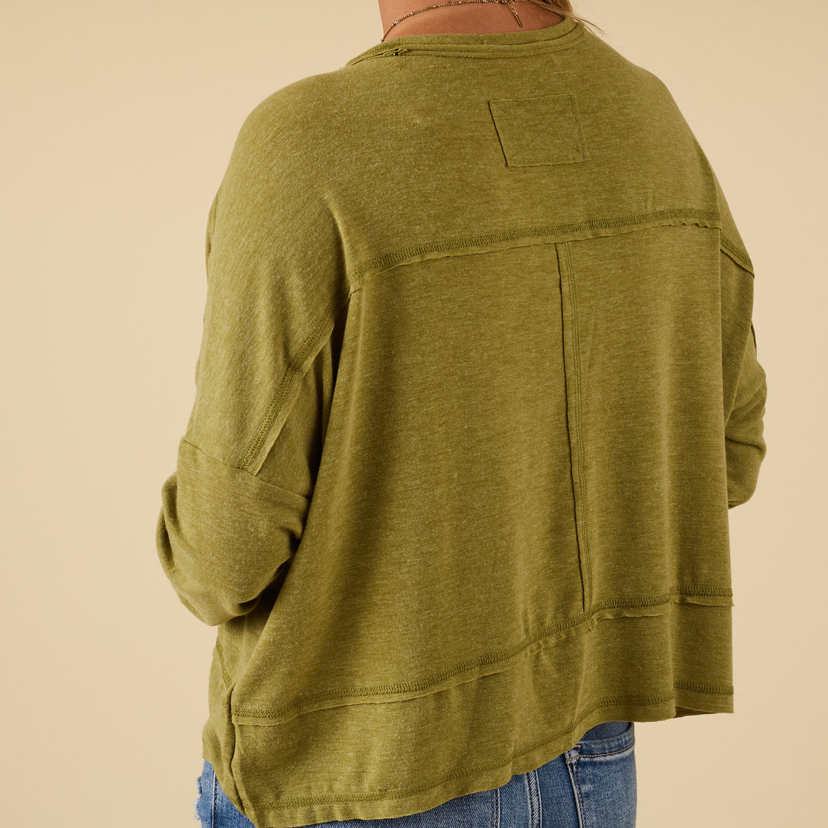 Back view of green long sleeve relaxed pocket top with raw seam accents and relaxed fit, styled with blue jeans.