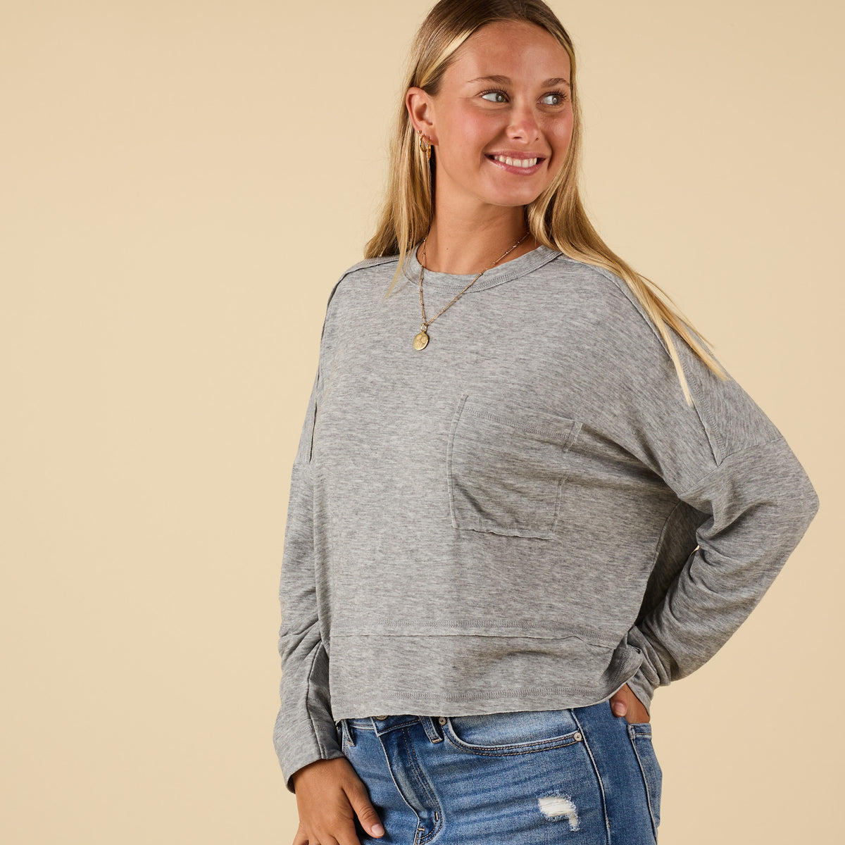 Side view of grey long sleeve relaxed pocket top with chest pocket and raw seam details, paired with jeans.