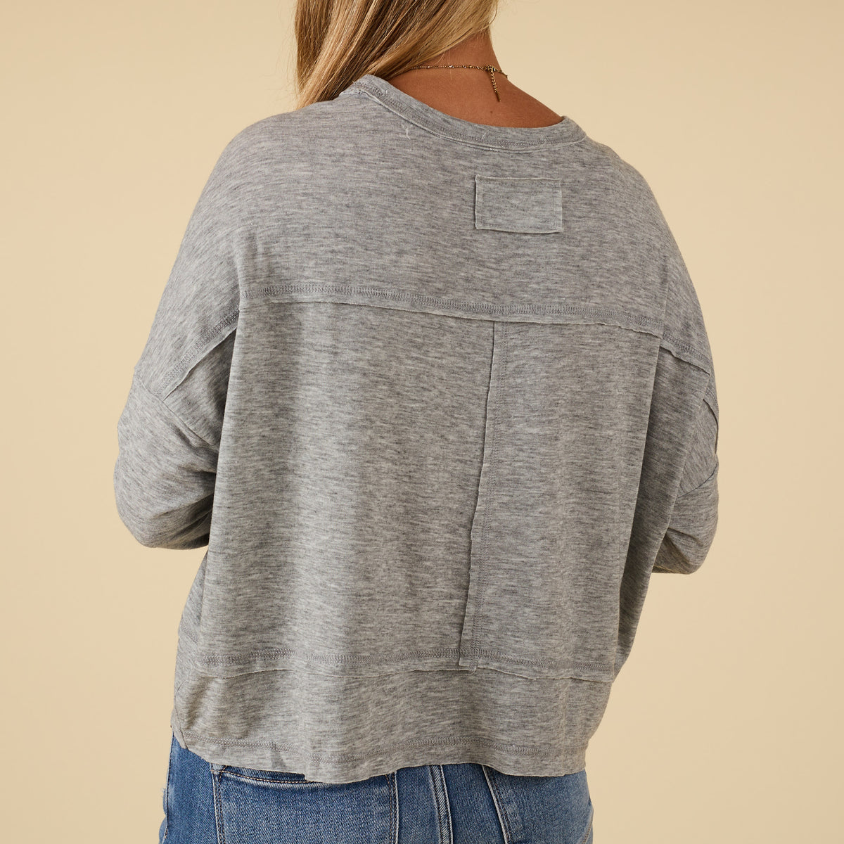 Back view of grey long sleeve relaxed pocket top with chest pocket and raw seam details, paired with jeans.