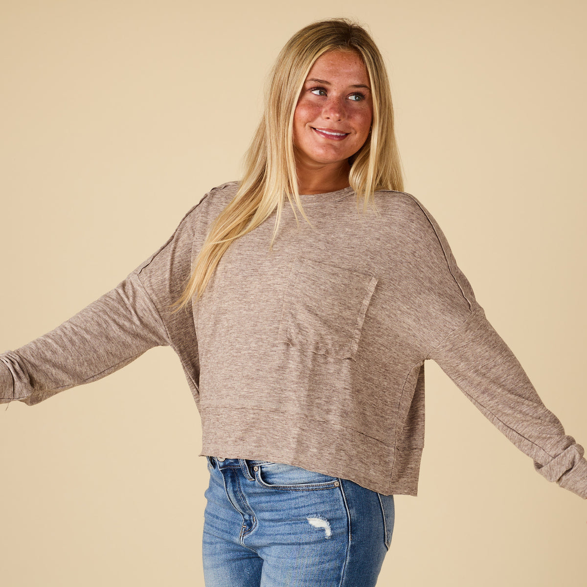 Side view of mocha long sleeve relaxed pocket top with raw seam detail and boxy relaxed fit, styled with light wash jeans.