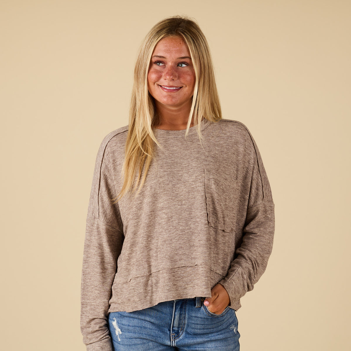 Front view of mocha long sleeve relaxed pocket top with raw seam detail and boxy relaxed fit, styled with light wash jeans.