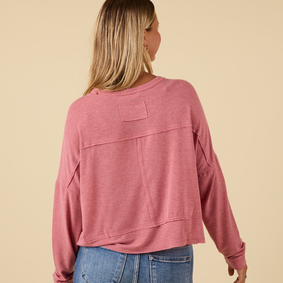 Back view of pink long sleeve relaxed pocket top with raw seam detail and boxy relaxed fit, styled with light wash jeans.