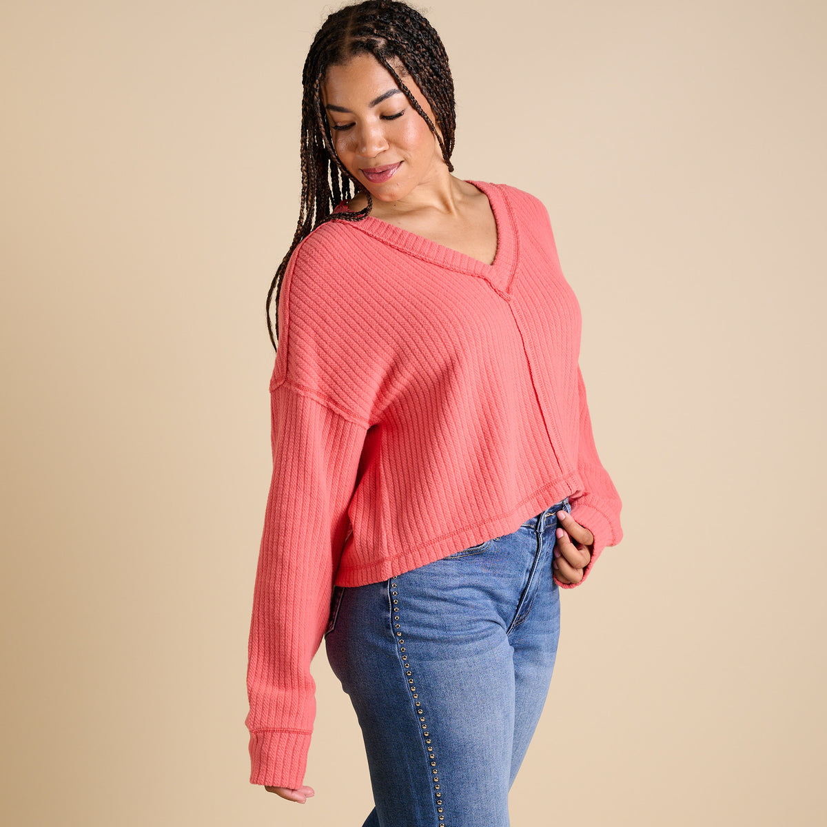 Model wearing coral ribbed V-neck cropped sweater with long sleeves and relaxed fit.