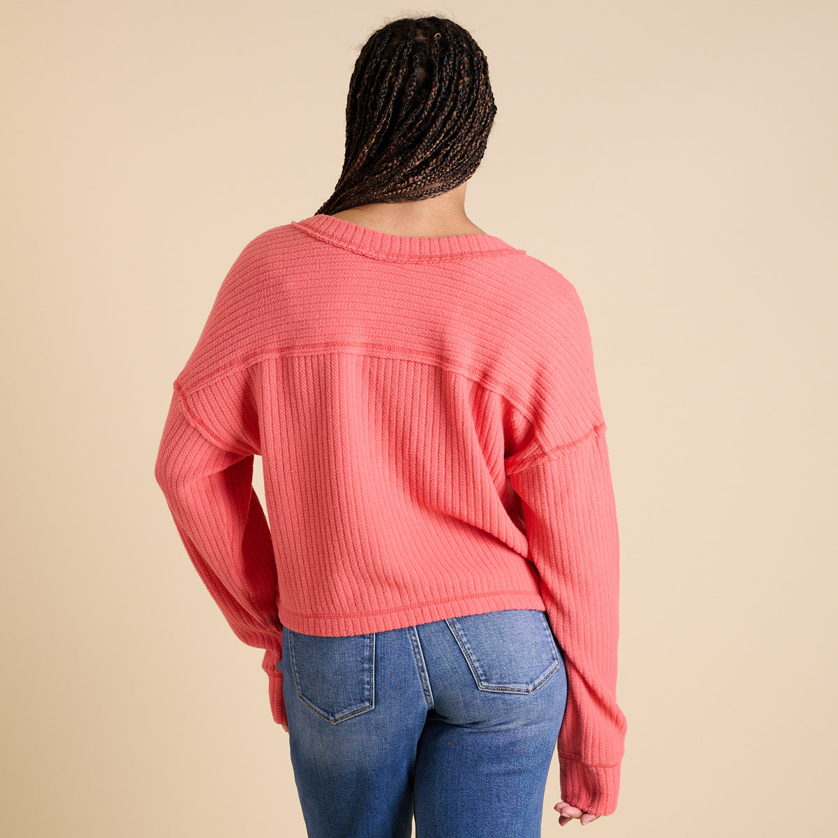 Model wearing coral ribbed V-neck cropped sweater with long sleeves and relaxed fit.