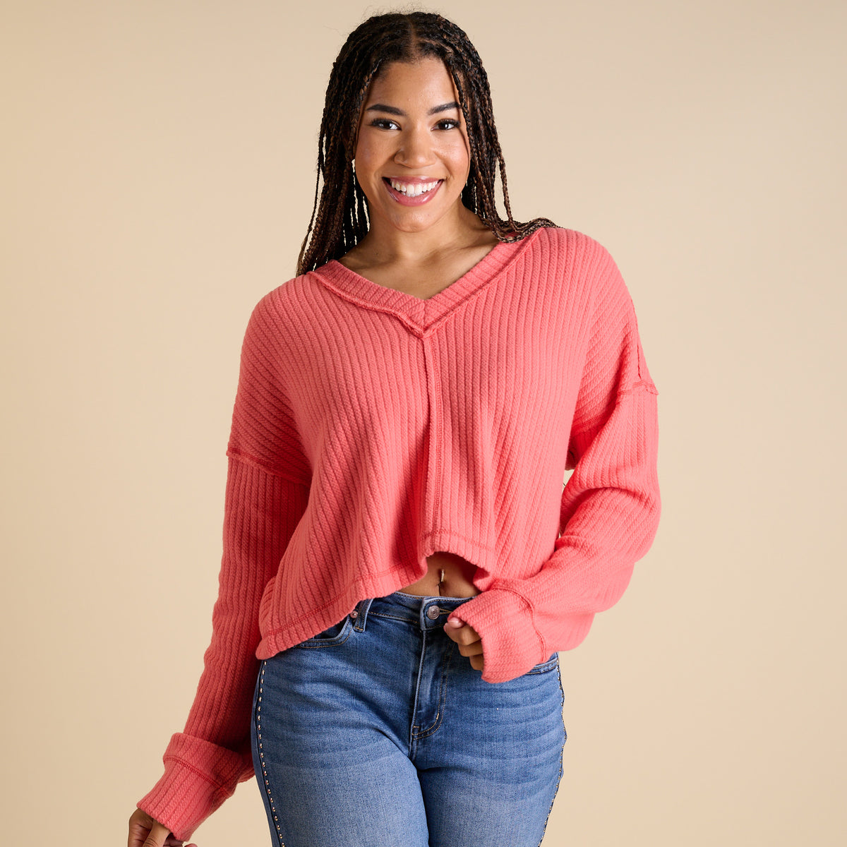 Model wearing coral ribbed V-neck cropped sweater with long sleeves and relaxed fit.