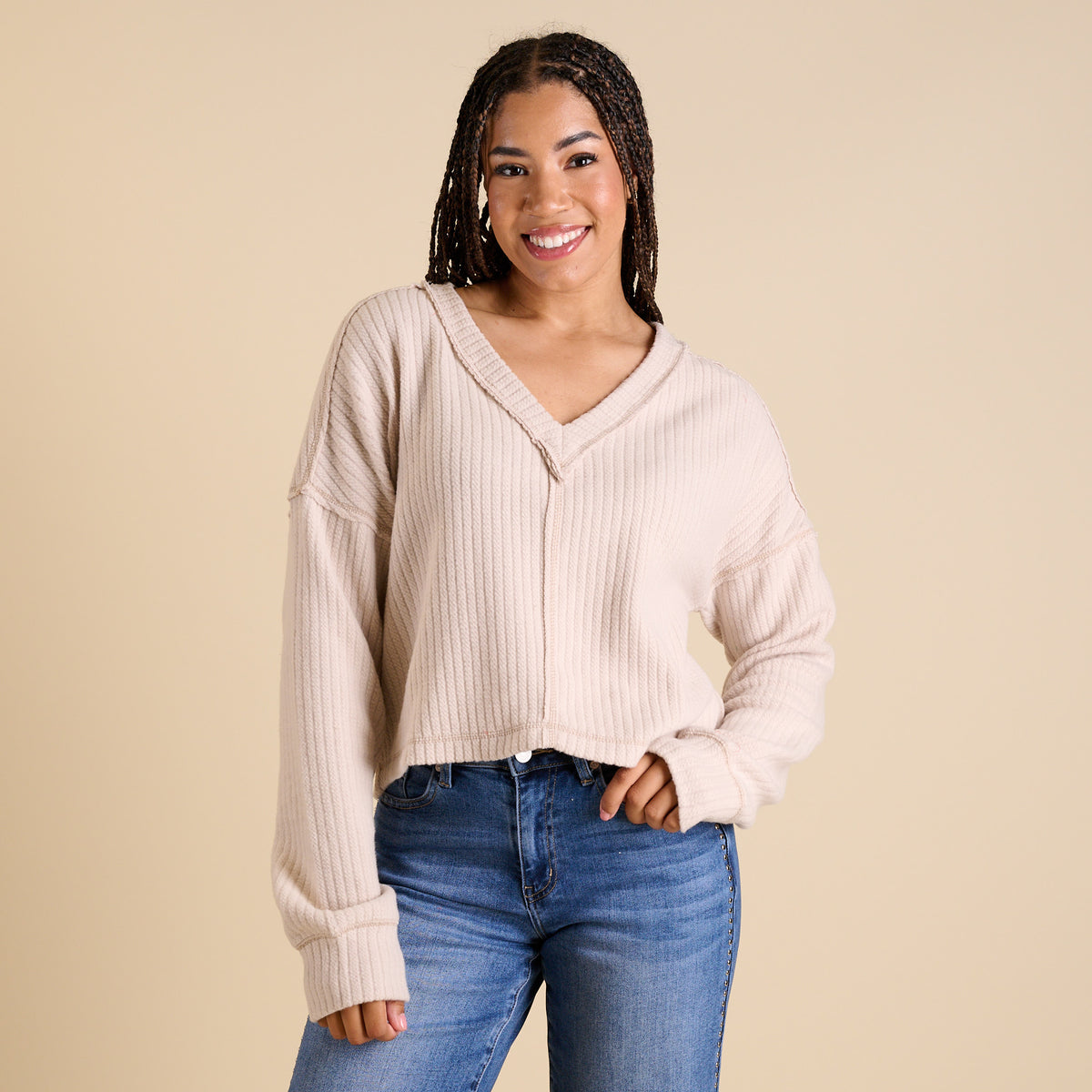 Model wearing ecru ribbed V-neck cropped sweater with long sleeves and relaxed fit.
