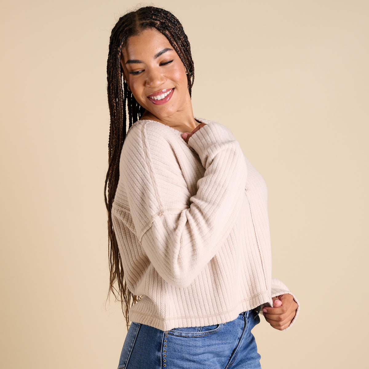 Model wearing ecru ribbed V-neck cropped sweater with long sleeves and relaxed fit.