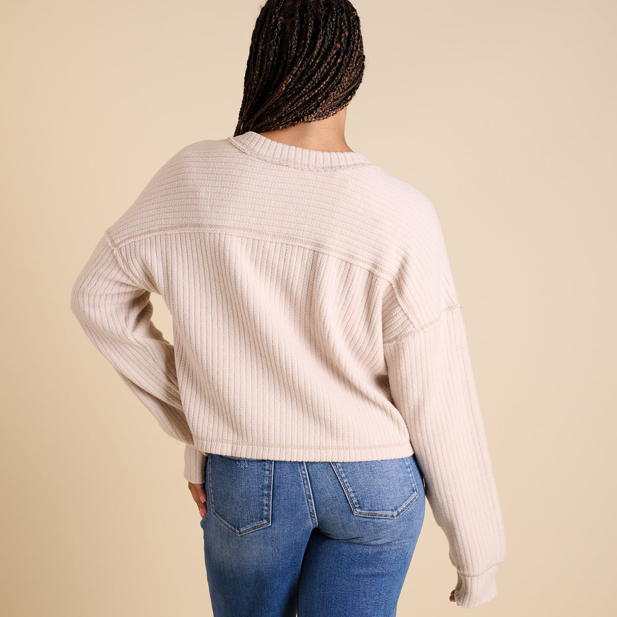 Model wearing ecru ribbed V-neck cropped sweater with long sleeves and relaxed fit.