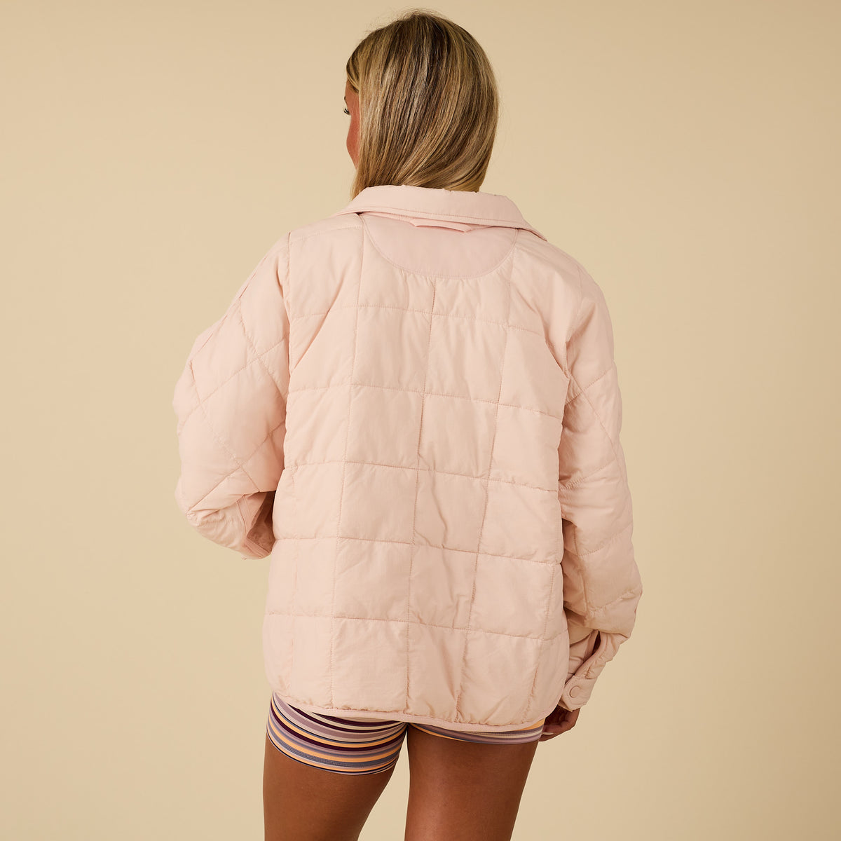 Person wearing a light pink quilted jacket on a beige background
