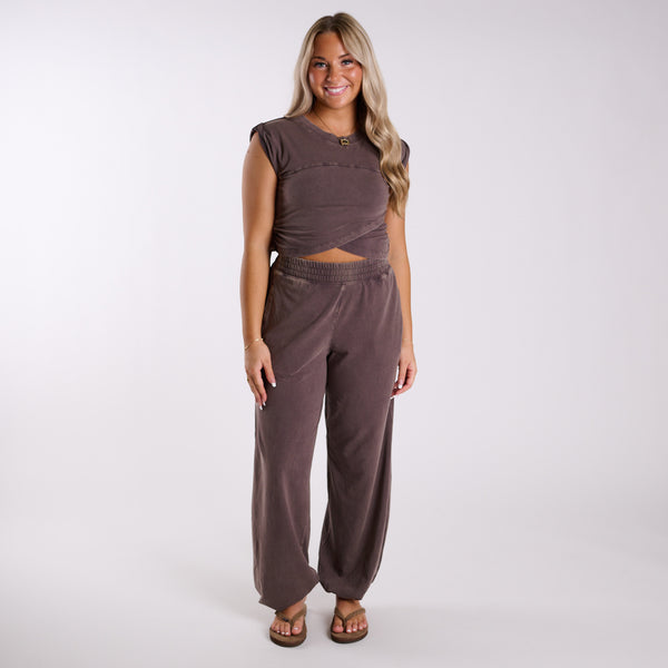 Chocolate brown two-piece lounge set shown from the front, featuring cropped twist-front top and relaxed elastic waistband pants.