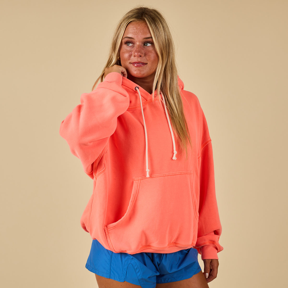 Front view of oversized neon coral hoodie with drawstrings and kangaroo pocket, styled with blue shorts.