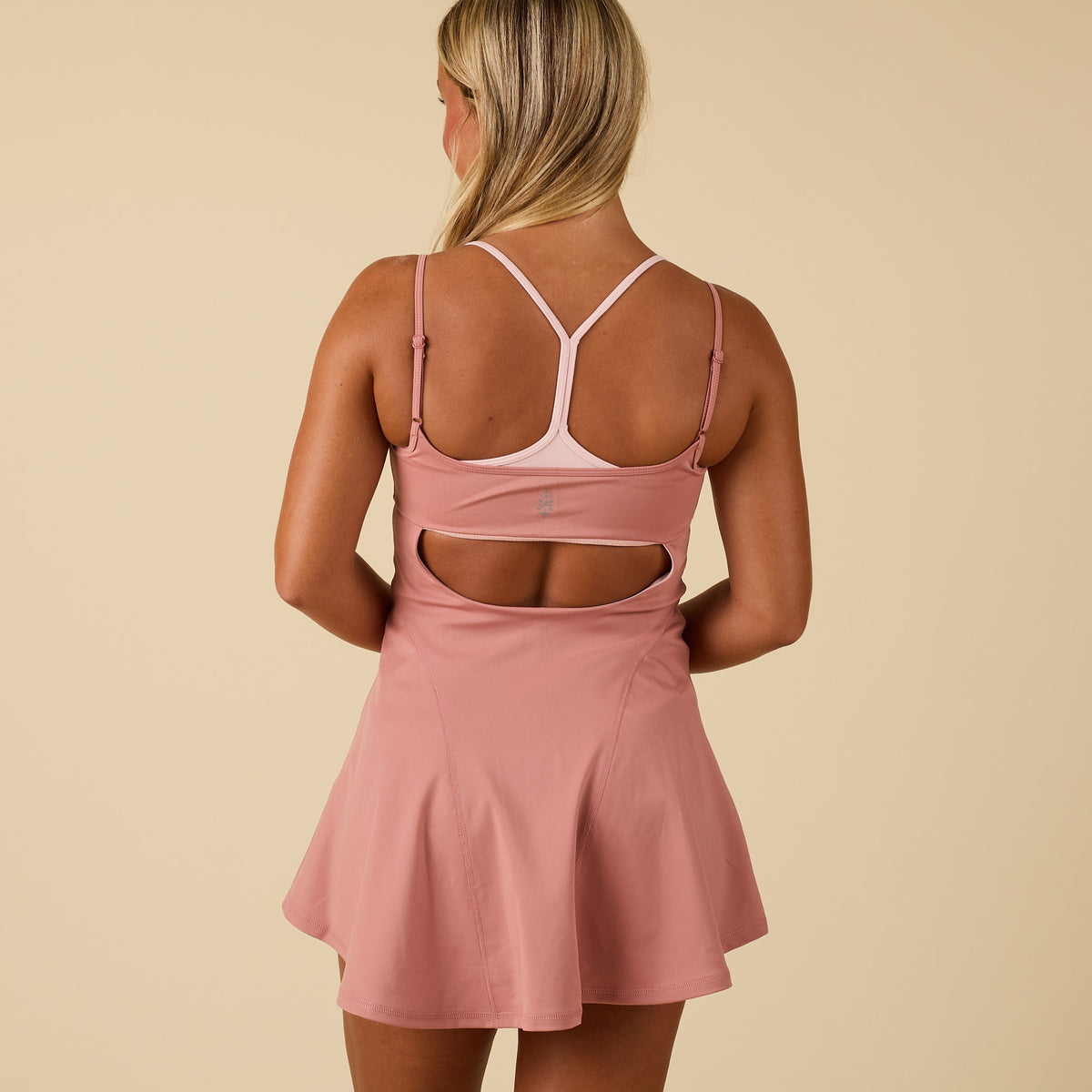 Back view of women’s pink athletic tennis dress with racerback straps and cutout detail above waist.