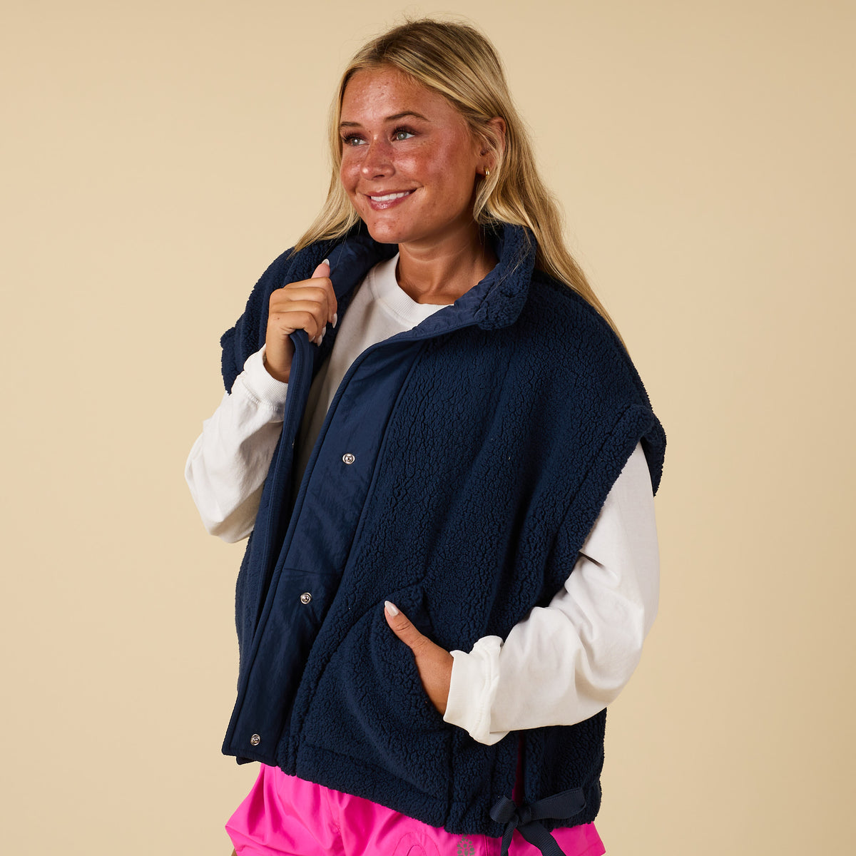 Front view of navy sherpa vest with snap buttons and side ties, worn over a white long sleeve.