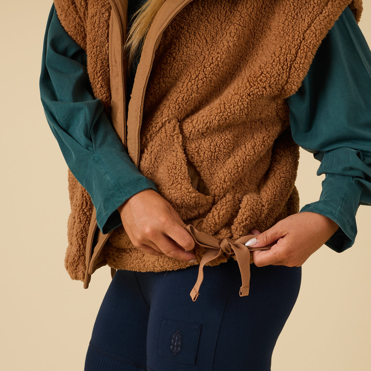 Close-up of side tie detail being adjusted on brown sherpa vest.